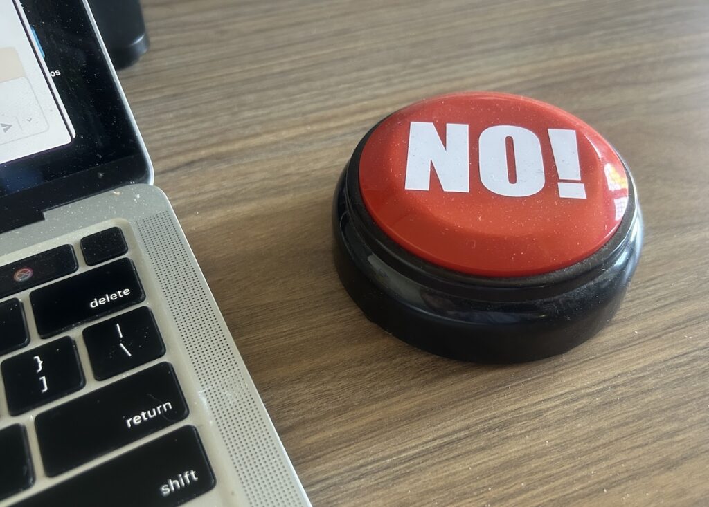 Large red button with the word "No!" on it, next to a laptop on a desk