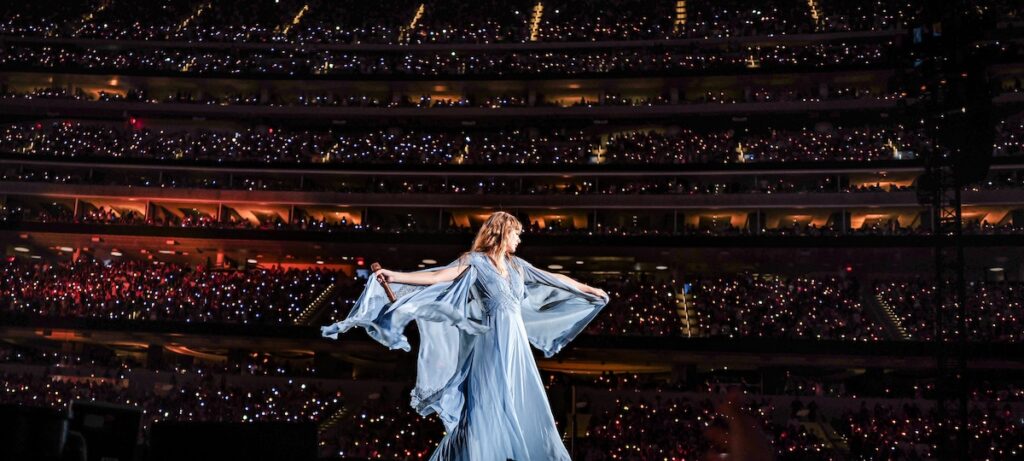 Taylor Swift on stage during the Eras Tour with the crowd's smartphones lighting up the seating area