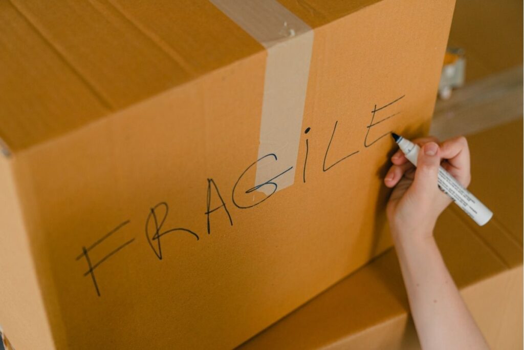 A woman's hand labelling a cardboard box with the word 'fragile'