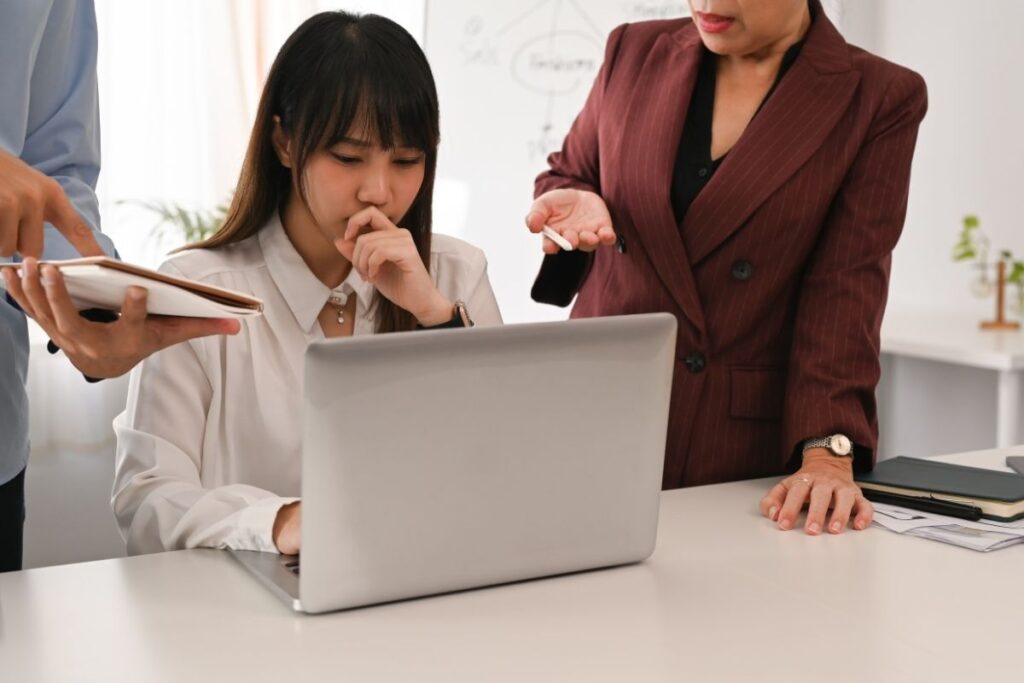 Nervous-looking young staffer at her computer while two more senior members of her team hover over her shoulder