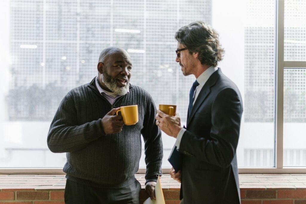 Two professionals having a quiet word over coffee at the window of an office building