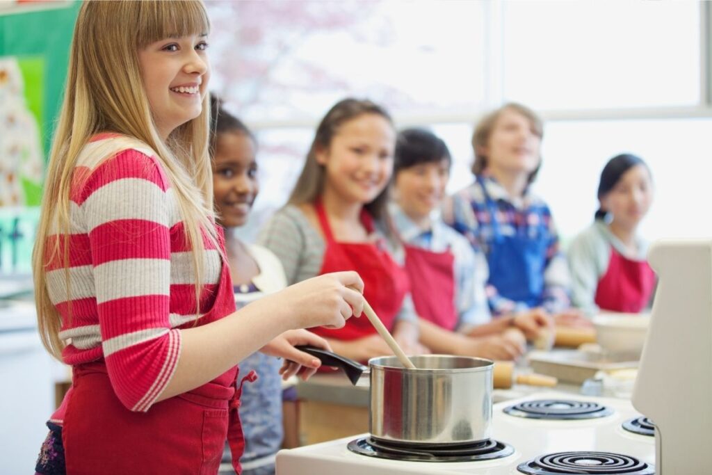 Students line up at a stove in a high school cooking class