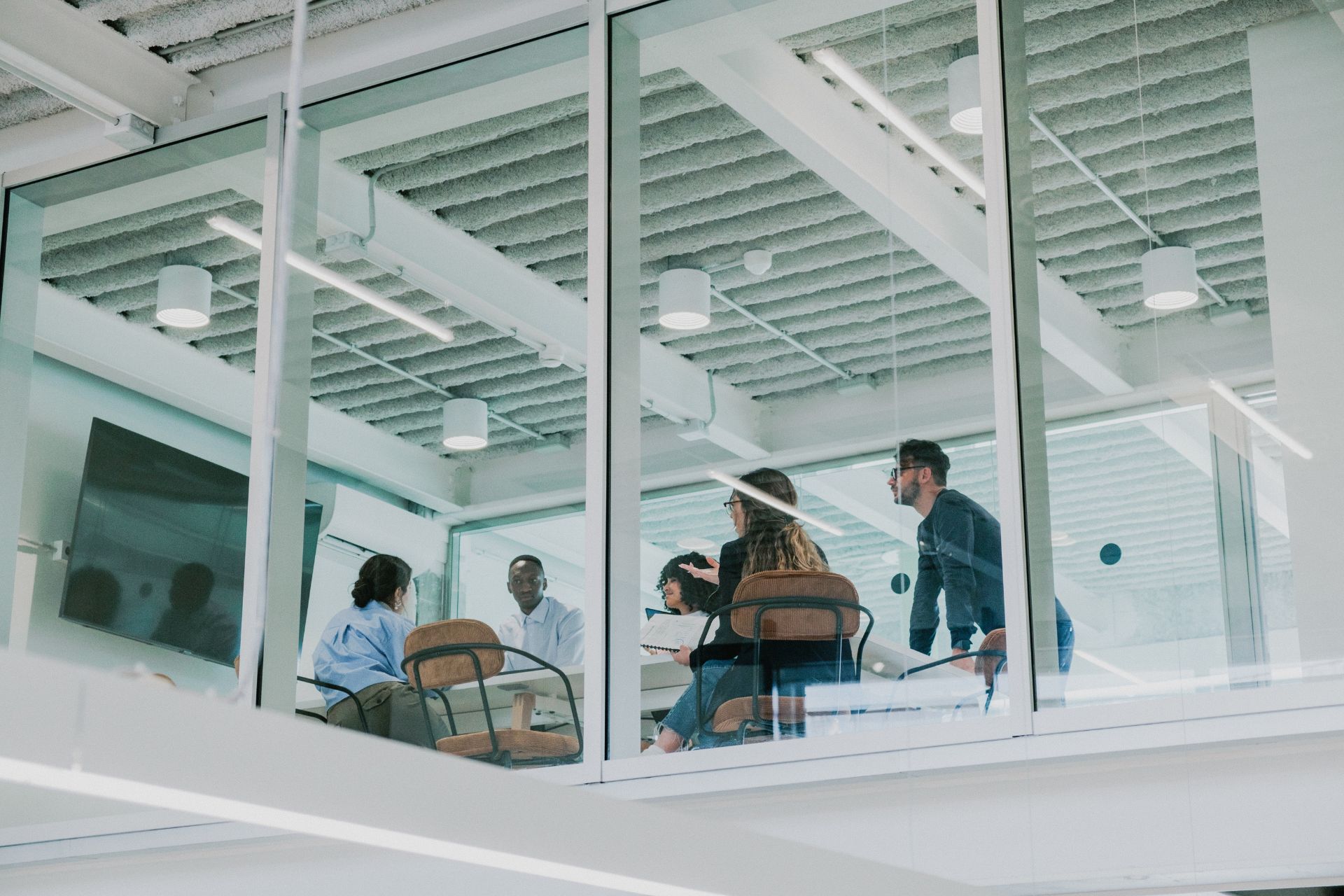 Group of communicators meet at a table, seen through the glass walls of a mezzanine boardroom from below.